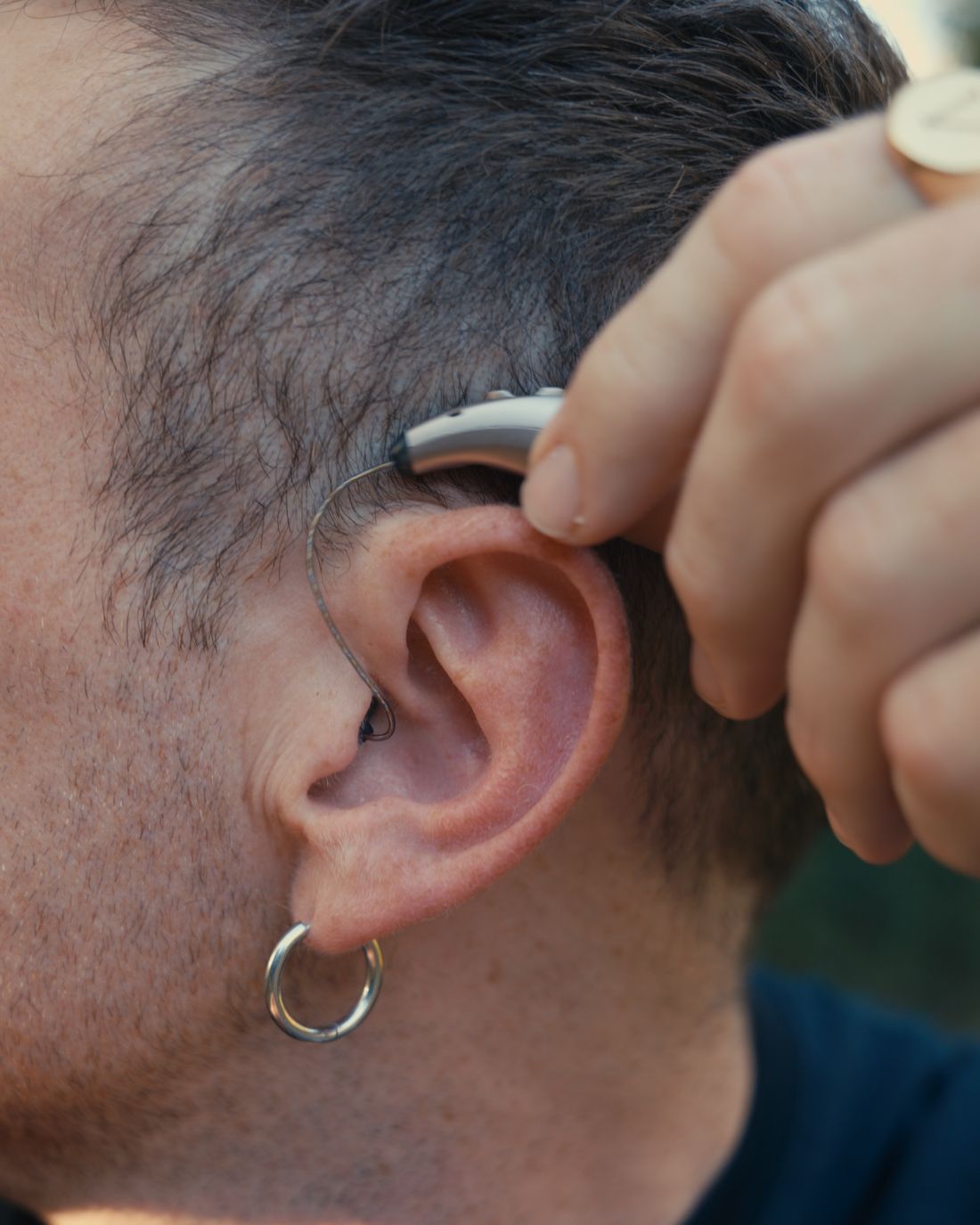 A finger pressing the button on a Clarion hearing aid worn behind the ear